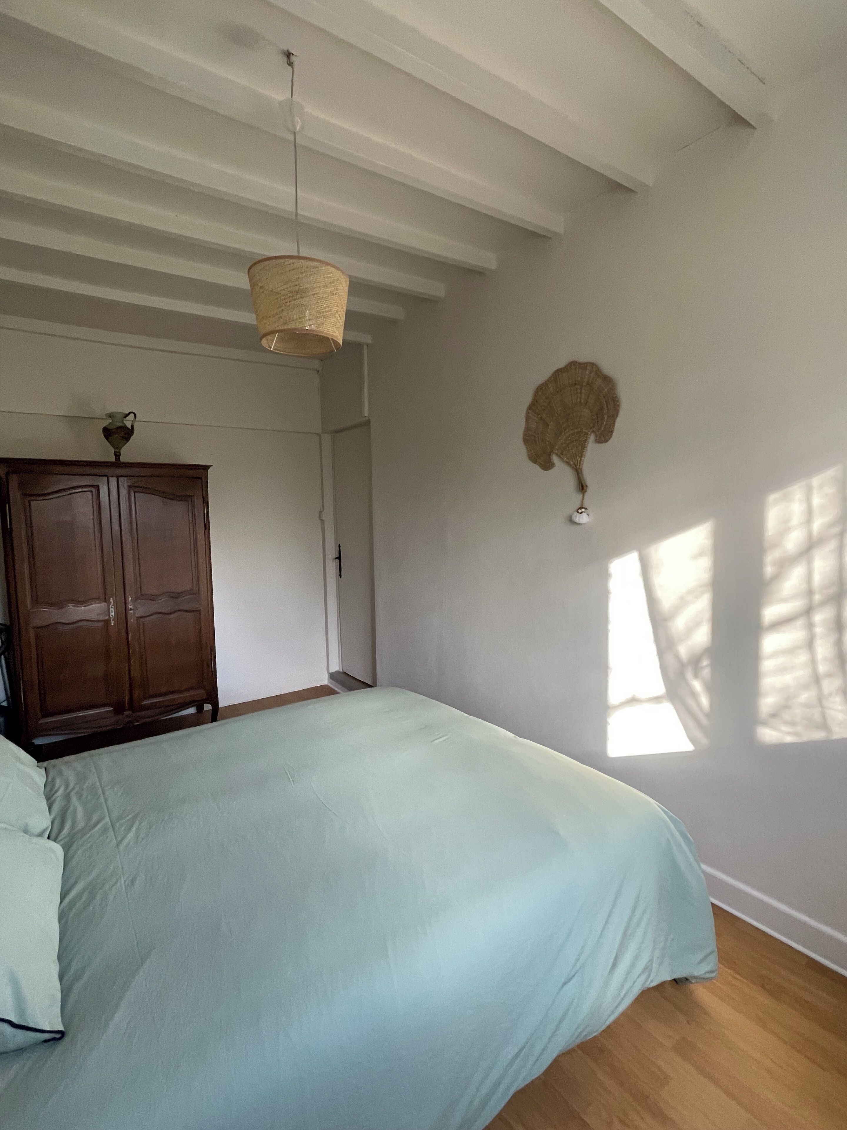 A bedroom with a bed, a wooden wardrobe, a hanging light fixture, and a wall decoration.
