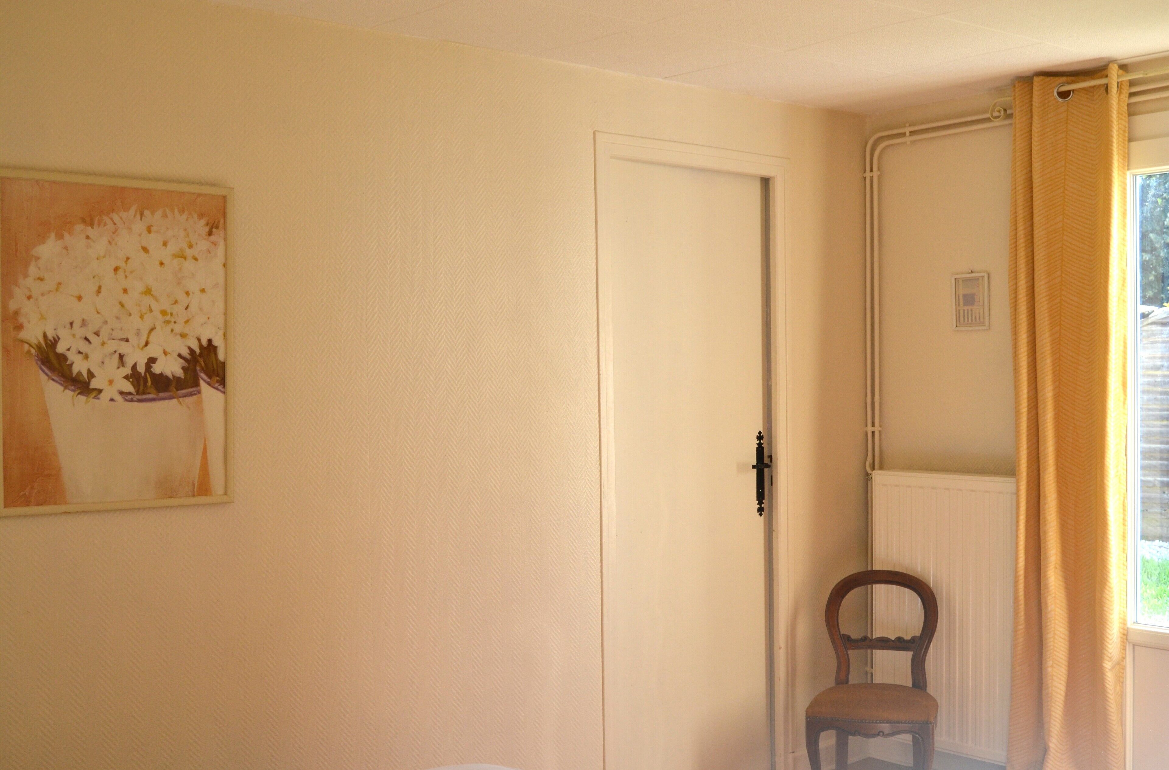 A room with a door, a radiator, a chair, and a window with curtains.