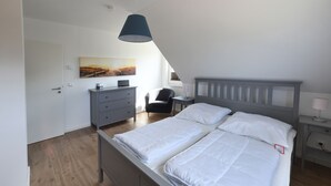 A bedroom with a bed, a desk, a chair, a dresser, a lamp, and a painting on the wall. - NEW 2018 holiday home exclusively near the beach, sauna, fireplace, free WiFi, garden (Wiek /Rügen)