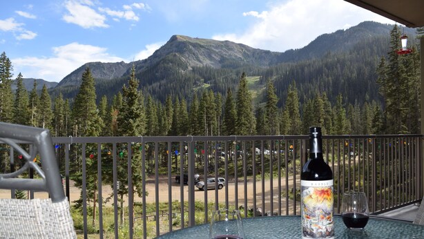 A glass table with a bottle of wine and a glass, set against a mountain backdrop.