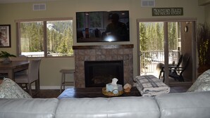A living room with a fireplace, a television mounted above it, and a sign above the fireplace that reads "Mountain Rules Ski Relax Enjoy."