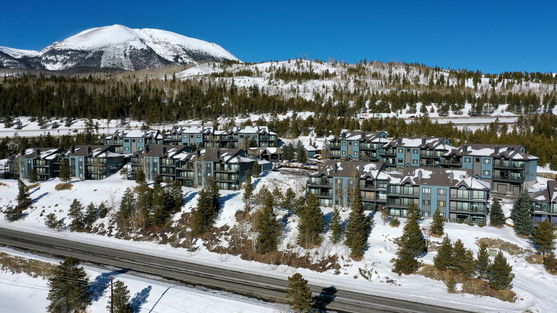 Une montagne enneigée sur laquelle se trouve un complexe hôtelier moderne, composé d’immeubles à plusieurs étages dotés de grandes fenêtres et de balcons.
