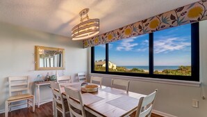 Un espace repas comprenant une table, des chaises, un lustre, un miroir et une grande fenêtre donnant sur l’océan.