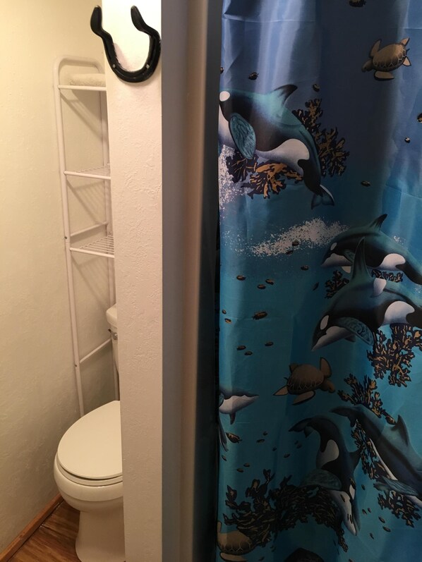 A bathroom with a white toilet, a white shelf unit, and a shower curtain with a marine life pattern.