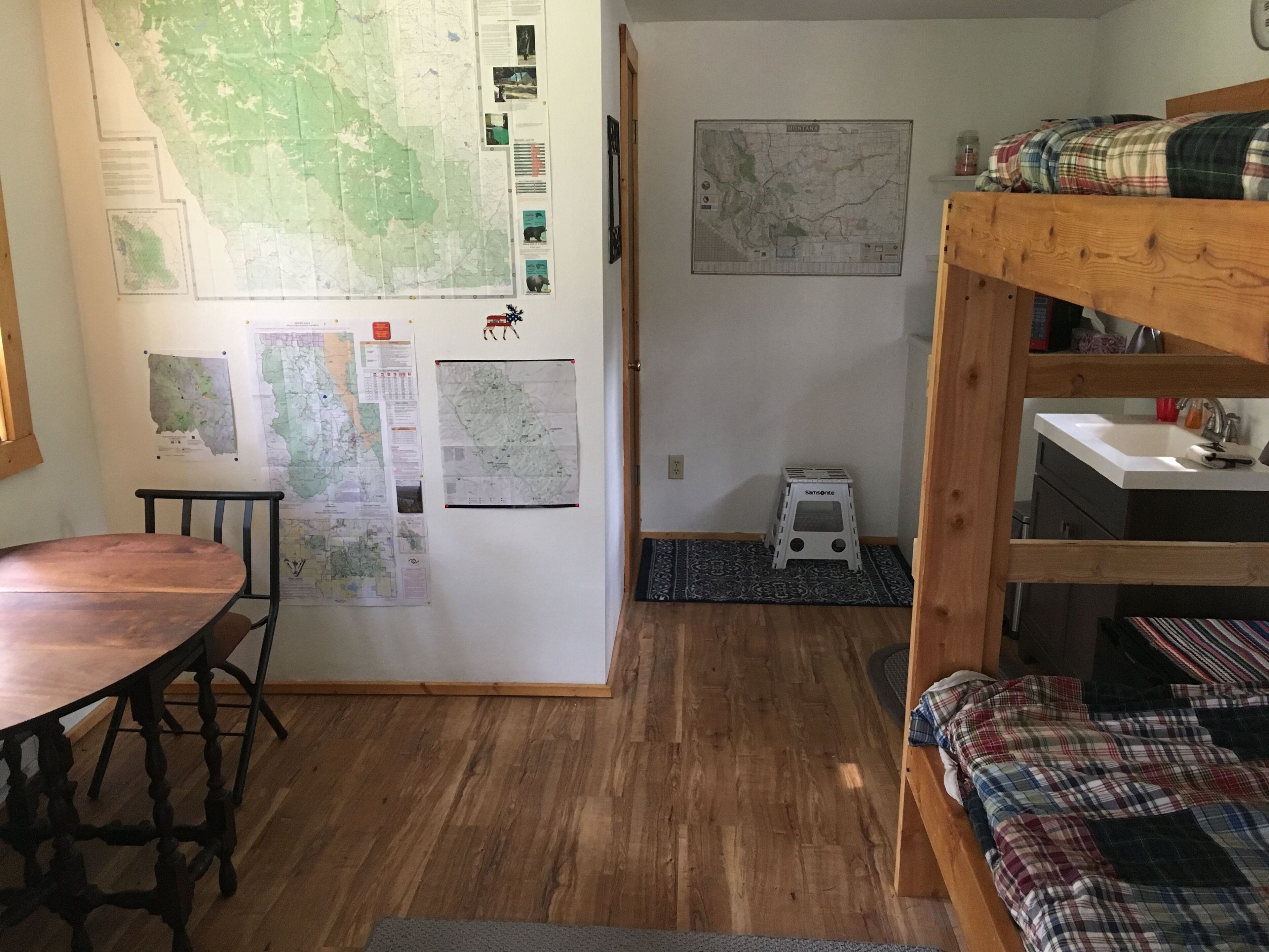 Une pièce avec un lit superposé, une table en bois et un bureau. Les murs sont ornés de cartes et d’affiches d’information.