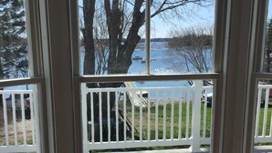 A bay window with a view of a lake and dock, a white railing, and a small wooden table with a book. - Historic "Wilbur Morse" Friendship Maine Ocean Home (Friendship)