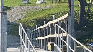 A wooden deck leading to a house with a white railing, a grassy yard, and outdoor furniture. - Historic "Wilbur Morse" Friendship Maine Ocean Home (Friendship)