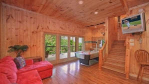L’intérieur d’un chalet en bois, avec un canapé rouge, une table de billard et un téléviseur diffusant un match de baseball.