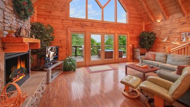 L’intérieur chaleureux d’un chalet en bois comprend une cheminée, un coin salon confortable et une grande porte vitrée donnant sur une terrasse extérieure.