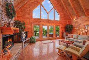 A cozy log cabin interior with a fireplace, a comfortable seating area, and a large glass door leading to an outdoor deck. - Most Unique Cabin in Smokies,HotTub+Gameroom Voted by Southern living Magazine! (Gatlinburg)