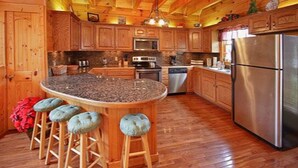 Une cuisine rustique, située dans une cabane en bois, avec un îlot central, des tabourets de bar, des appareils en acier inoxydable et des armoires en bois.