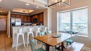 A modern kitchen with wooden cabinets, a stainless steel refrigerator, and a large island with bar stools.