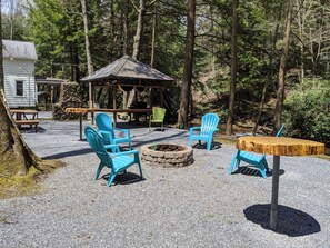 Ein rustikaler Sitzbereich im Freien mit Adirondack-Stühlen, einem Holztisch und einem Steinkamin.