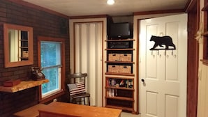 A cozy room with a brick wall, a wooden bench, a television on a shelf, and a bear-shaped wall decoration. - Montgomery Run cabin located in a secluded wooded area close to Clearfield, PA (Clearfield)