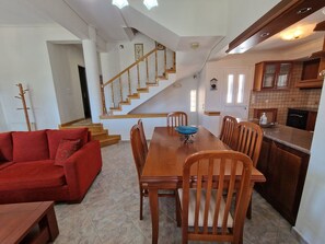 A spacious living area with a wooden dining table, red sofa, and a staircase leading to an upper floor. - The Mirador Boutique Villa with Scenic Sea View (Porto Rafti)
