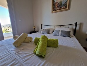 A neatly made bed with white and green towels, a painting on the wall, and a nightstand with a lamp. - The Mirador Boutique Villa with Scenic Sea View (Porto Rafti)