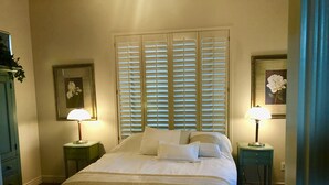 A neatly made bed with white linens, flanked by two bedside tables with lamps, a large window with blinds, and a framed picture on the wall. - Casita Del sol, 1 BR 1BA-Sleeps 2. Minimum Stay 4 nights. Great North Phoenix (Phoenix)