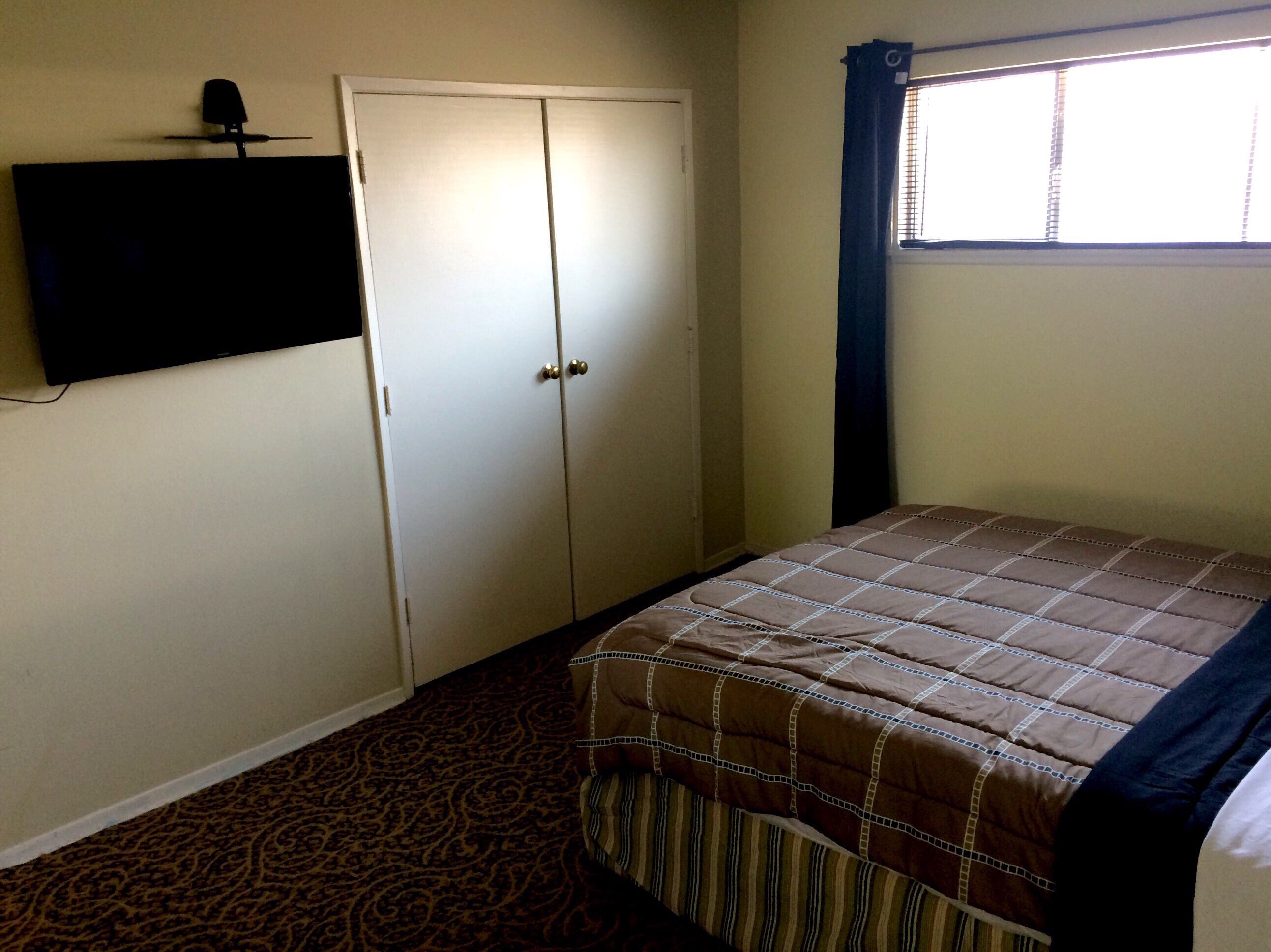 A bedroom with a bed, a wardrobe, a television mounted on the wall, and a window with curtains.