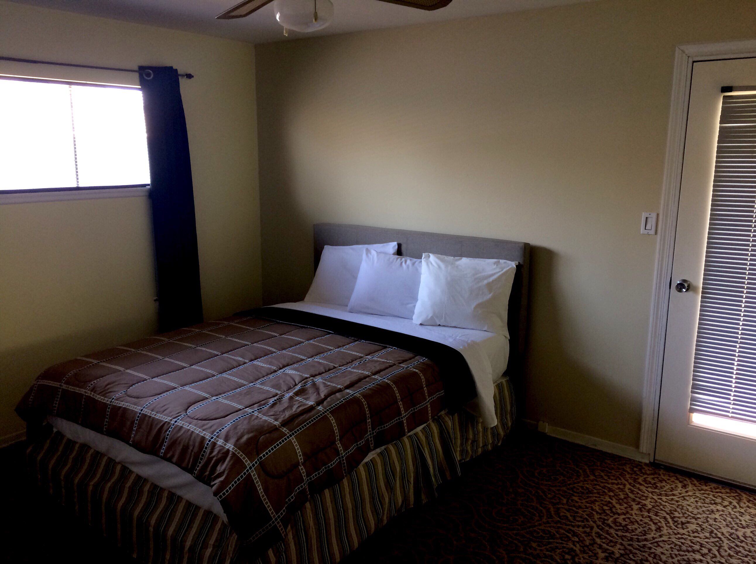 A bedroom with a bed, a window with curtains, a door, and a carpeted floor.