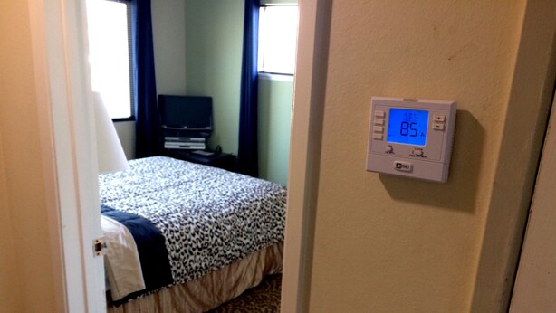 A bedroom with a bed, a thermostat, and a window.
