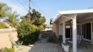 A covered patio area with a seating arrangement, a small garden with gravel and plants, and a white fence.
