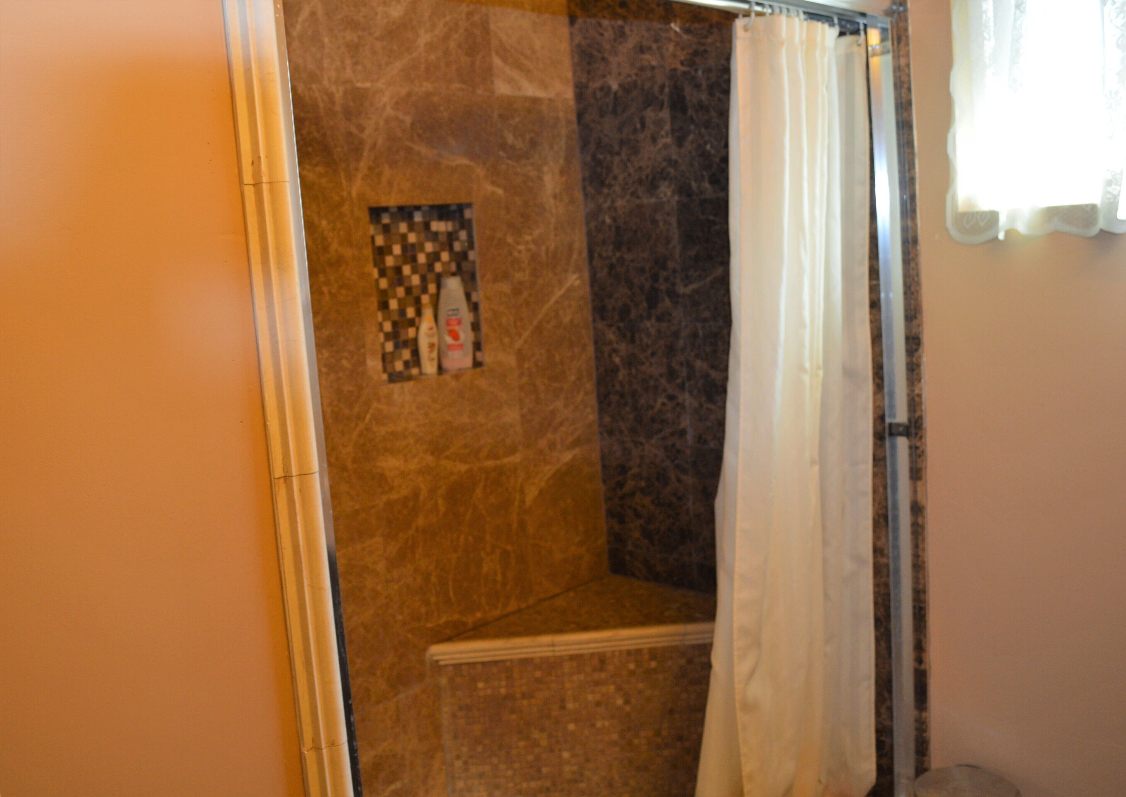 Un área de ducha con pared de baldosas a cuadros, una cortina de ducha y piso de azulejos.
