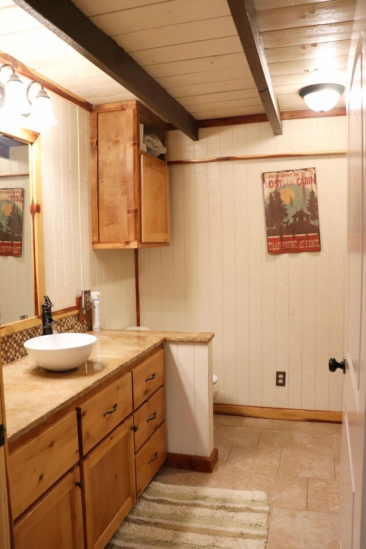 A bathroom with wooden cabinets, a white sink, and a poster on the wall.