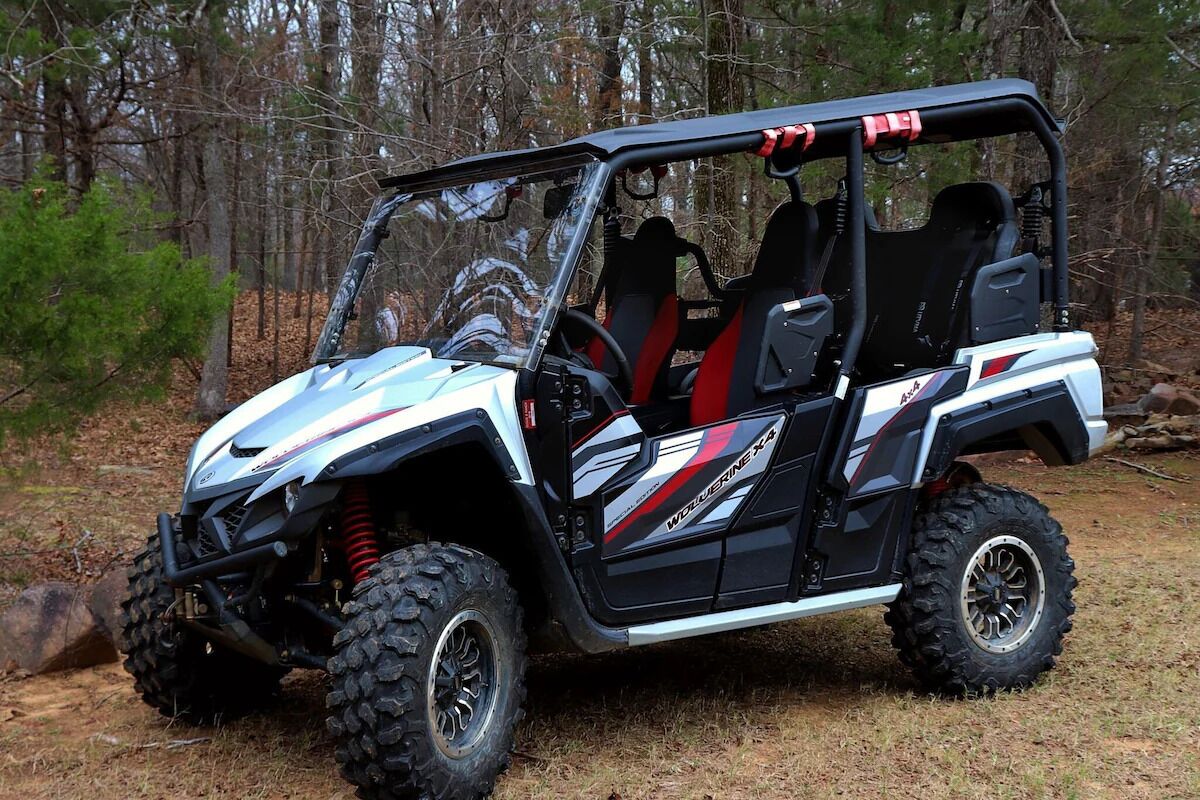 A white and black off-road vehicle with red accents and large tires, parked in a wooded area.