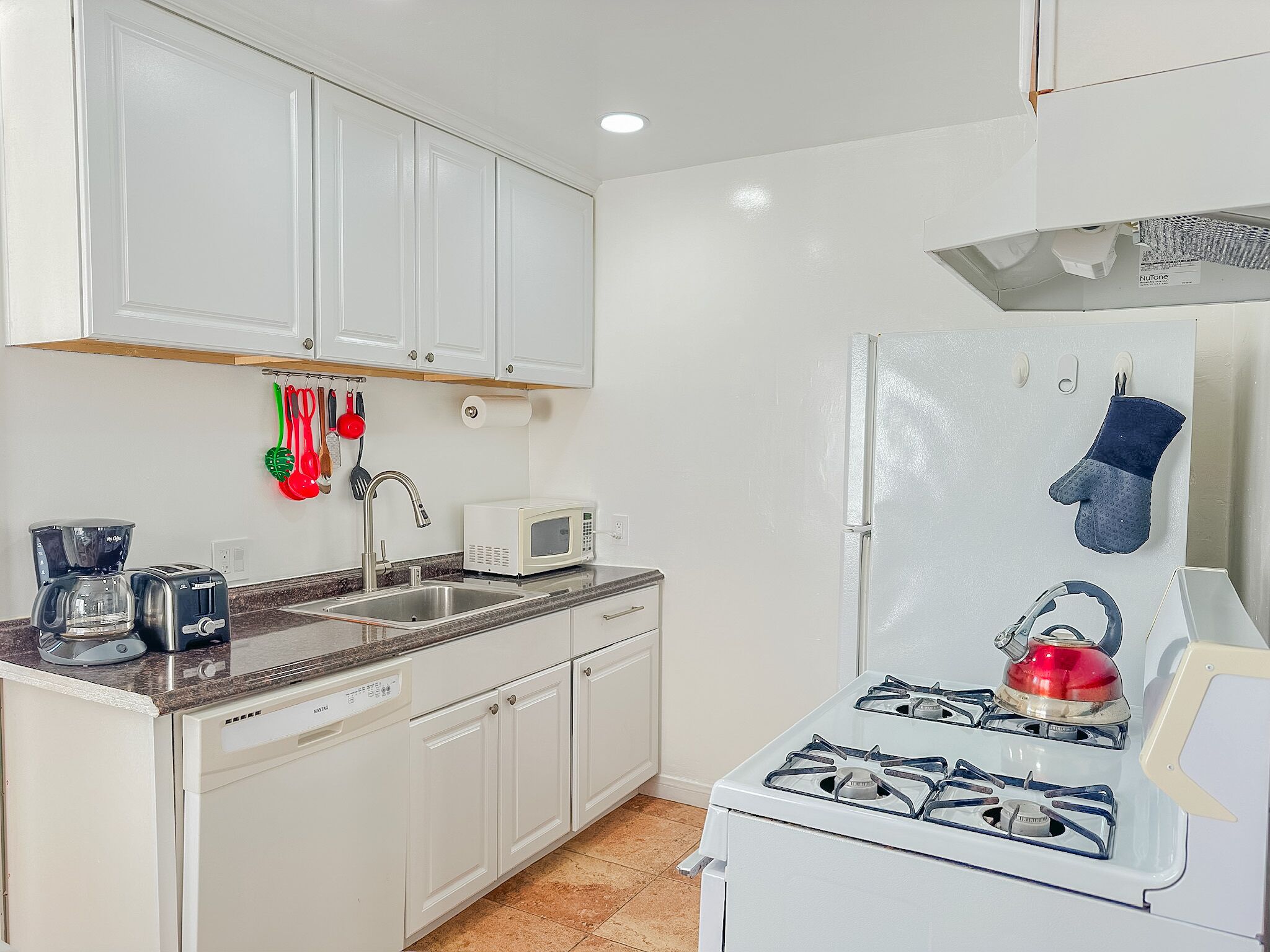 A compact kitchen with white cabinets, a sink, a microwave, a gas stove, and a kettle.