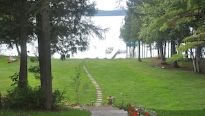 A pathway leading to a lake with a dock, surrounded by trees and a well-maintained lawn. - Sunsets,140' on Torch Lk,Lg Dock,Hot Tub,Tennis/Pickle Crt,Kayaks,Play/swing set (Bellaire)