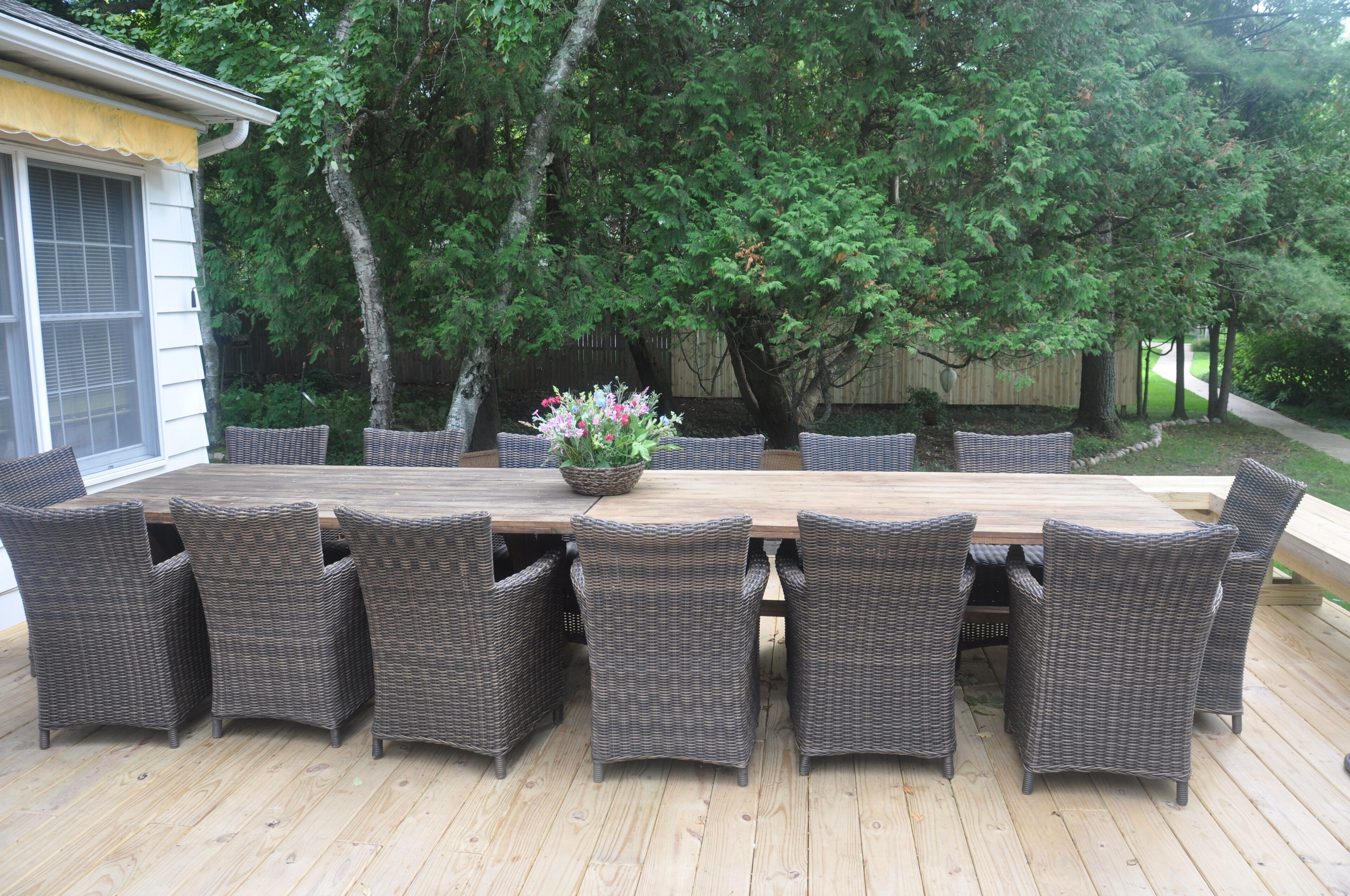 A wooden deck with a large dining table surrounded by wicker chairs.