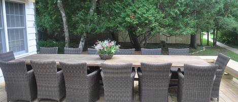 A wooden deck with a large dining table surrounded by wicker chairs.