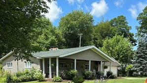 Une maison de plain-pied dotée d’un porche à l’avant, entourée d’une pelouse bien entretenue et de divers arbustes.
