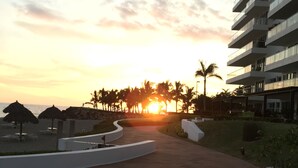 Un complexe hôtelier offrant une vue sur le coucher de soleil, des palmiers et un bâtiment moderne doté de balcons.