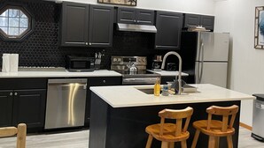 Une cuisine moderne avec des meubles de couleur noire, des appareils en acier inoxydable et un îlot central doté de tabourets de bar.