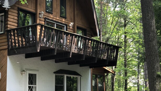 Une cabane en rondins dotée d’un balcon, entourée d’arbres.