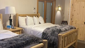 Une chambre à coucher avec deux lits en bois, un ventilateur de plafond, une table de chevet avec une lampe et une porte.