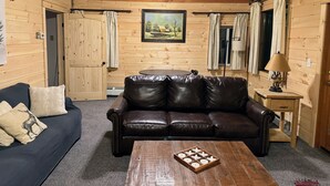L’intérieur chaleureux d’un chalet avec un canapé en cuir, une table basse en bois et un ventilateur de plafond.