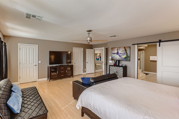 Une chambre moderne avec un grand lit, une télévision, un ventilateur de plafond et un placard à portes coulissantes.