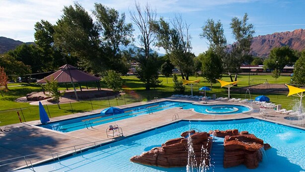 A swimming pool with a waterfall feature, surrounded by lounge chairs and shaded areas, set against a mountainous backdrop. - Super Affordable & Spacious 3 BR Townhouse w/3 en-suite baths (Moab)