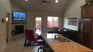 A modern kitchen with a granite countertop, stainless steel appliances, and a dining area with a red chair and a TV mounted on the wall. - Super Affordable & Spacious 3 BR Townhouse w/3 en-suite baths (Moab)