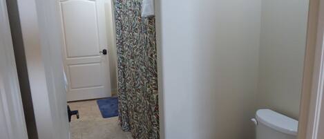 A bathroom with a toilet, a shower curtain with a leaf pattern, and a blue mat on the floor.