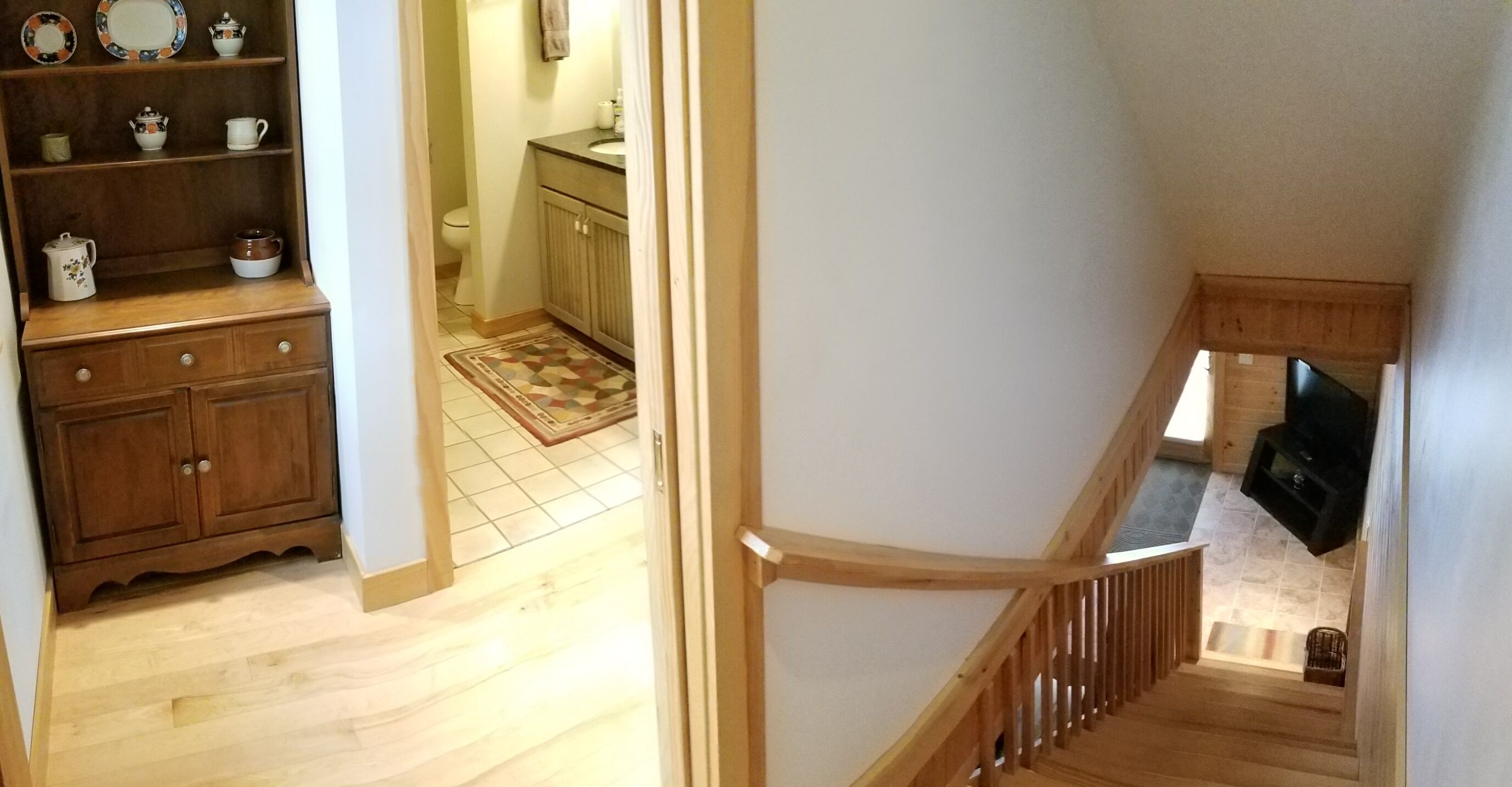 A wooden staircase with a handrail and a TV mounted on the wall at the bottom.