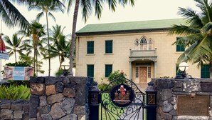 A stone wall with a wrought iron gate leading to a building with a green roof and a balcony.