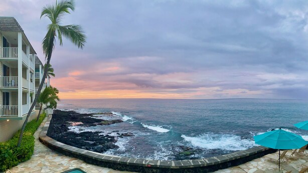 A pool area with a view of the ocean and a building with balconies.