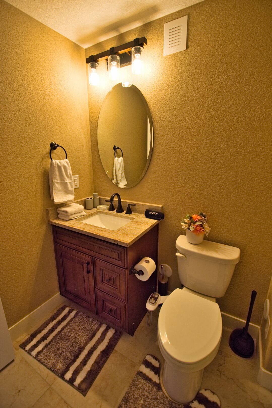 A bathroom with a sink, mirror, toilet, and a small potted plant.