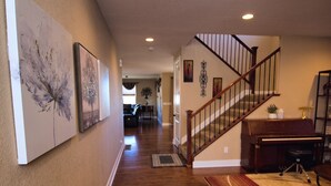 A spacious hallway with hardwood flooring, a staircase, and a piano. - Charming 6-BR Home with Open Space & Park, Ideal for Gatherings (Parker)
