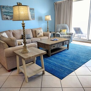 A living room with a sofa, two coffee tables, and a chair. There are two lamps on the tables.