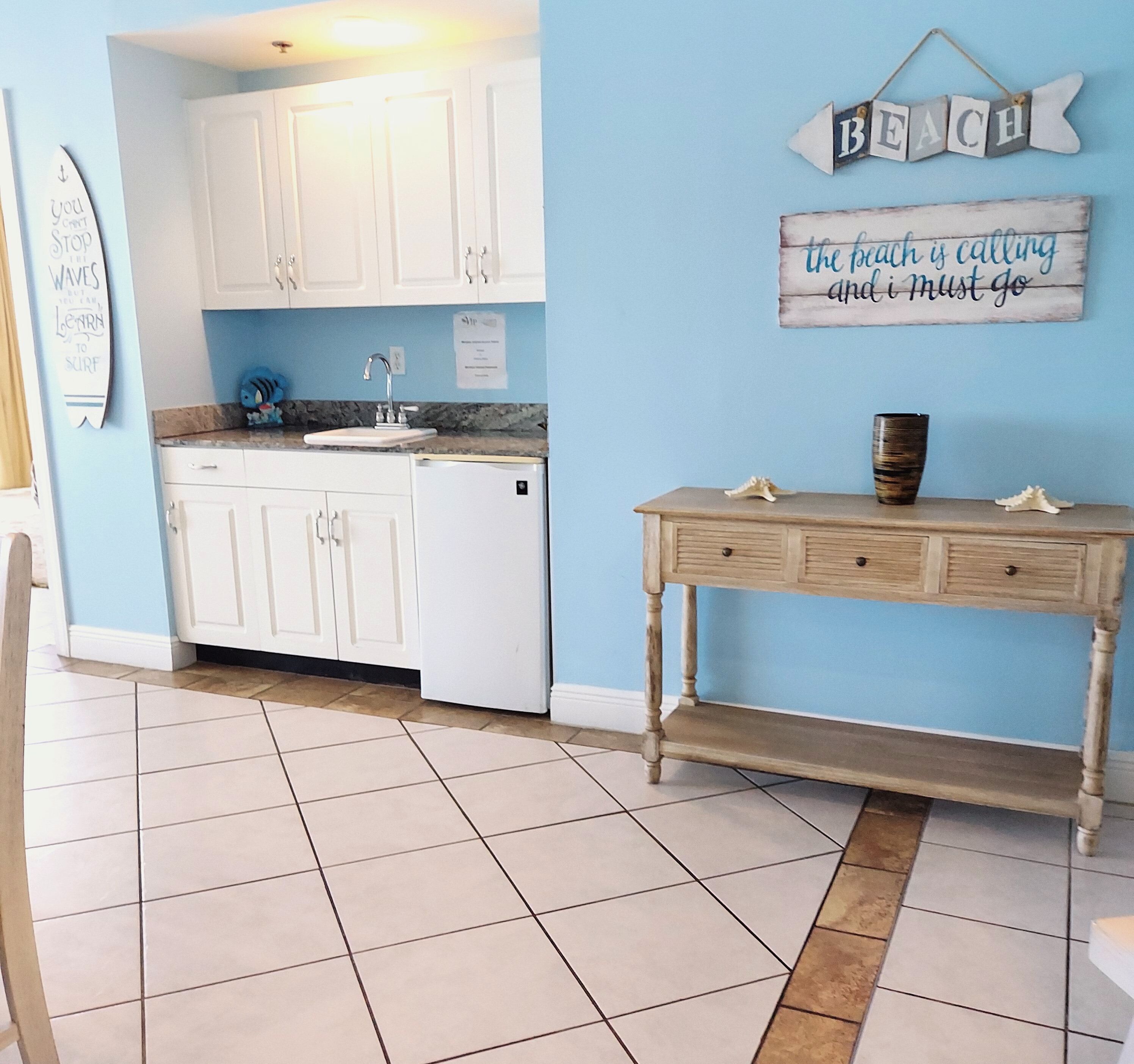 Une cuisine avec des meubles blancs, un évier et une console en bois ornée de coquillages décoratifs.