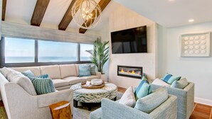 A modern living room with a large window, a fireplace, and a ceiling with exposed beams.